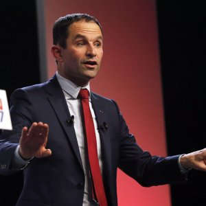 "Stasera la sinistra rialza la testa". Benoît Hamon saluta così i militanti radunati alla Mutualité nel quinto arrondissement. E' lui, 49 anni, il candidato del partito socialista all'Eliseo. Hamon trionfa nelle primarie con il 58% dei voti rispetto al 41% dell'avversario Manuel Valls. L'ex premier è stato battuto con un largo scarto, pagando l'eredità del suo governo e l'impopolarità di François Hollande. Valls ha augurato "buona fortuna" al suo rivale che, con poco fair play, l'ha interrotto mentre stava salutando i suoi sostenitori. Il candidato prescelto, su cui nessuno o quasi avrebbe scommesso fino a qualche settimana fa, è il simbolo di una svolta verso la base più radicale della sinistra. Il suo programma è stato definito dall'avversario "utopico": orario di lavoro a 32 ore settimanali, reddito universale per tutti i cittadini pagato dallo Stato, nuova tassa sui robot per le imprese. Il "Sanders alla francese" rappresenta un ritorno al "socialismo rivoluzionario" di altri tempi dopo cinque anni di esercizio di governo che hanno profondamente spaccato la gauche. "Dobbiamo immaginare risposte nuove, riflettere sul mondo per com'è e non per com'era" ha spiegato Hamon nel discorso di vittoria, con la mano sul cuore, il gesto diventato il suo marchio di fabbrica e lo slogan della sua campagna ("Far battere il cuore della Francia"). "Vogliamo vincere" ha promesso ancora Hamon, nonostante i sondaggi siano per lui poco favorevoli. Il candidato del Ps deve affrontare una forte concorrenza sull'estrema sinistra: sia il gauchiste Jean-Luc Mélenchon che il verde Yannick Jadot. E' a questi concorrenti diretti che ha lanciato un primo appello per aprire un "dialogo", con la speranza che almeno uno dei due faccia desistenza. I sondaggi prevedono infatti finora l'eliminazione sicura di Hamon al primo turno delle presidenziali del 23 aprile. Il nuovo candidato non ha invece detto una parola su Emmanuel Macron, altro avversario che mette a repentaglio le chances del socialista. Il candidato centrista è il grande vincitore politico di queste primarie, alle quali non ha mai voluto partecipare. Adesso può sperare di ottenere il voto degli elettori di sinistra più moderati, delusi dalla sconfitta di Valls. L'uscita di scena dell'ex premier potrebbe provocare una fuoriuscita di voti e persino di dirigenti dal Ps verso il movimento "En Marche" di Macron, anche se è ancora presto per calcolare i rapporti di forza tra i nuovi equilibri.